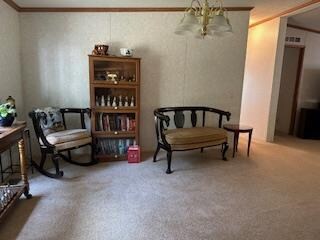 sitting room with a notable chandelier, ornamental molding, and carpet