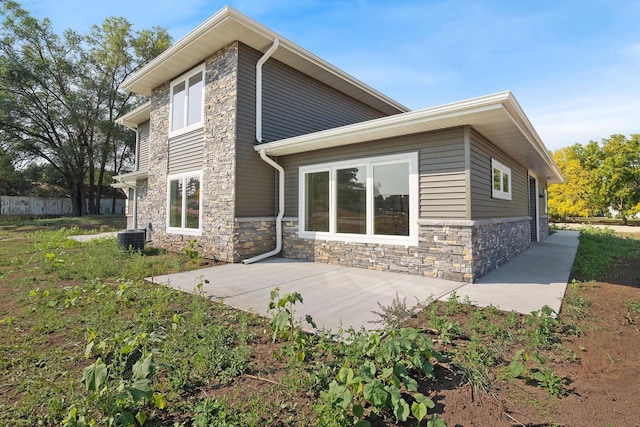 rear view of house with stone siding and central AC