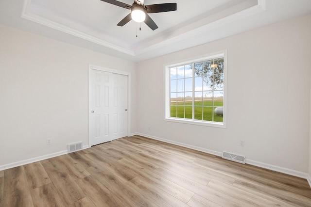 unfurnished room featuring a tray ceiling, ceiling fan, light hardwood / wood-style floors, and crown molding