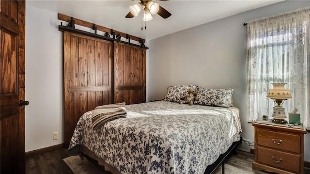 bedroom with ceiling fan, dark hardwood / wood-style floors, and a barn door