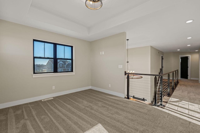 empty room featuring a chandelier, a raised ceiling, and carpet