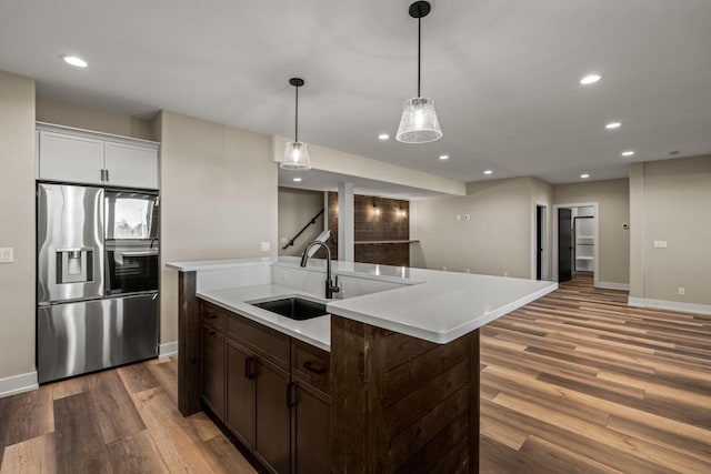 kitchen with dark brown cabinetry, sink, stainless steel fridge with ice dispenser, an island with sink, and hardwood / wood-style floors