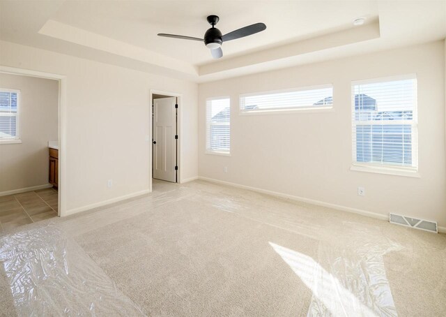 unfurnished bedroom featuring a raised ceiling, ceiling fan, and multiple windows