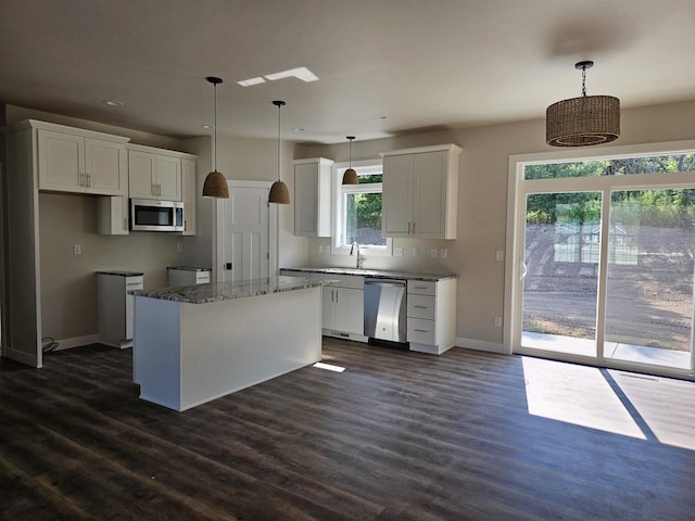 kitchen featuring appliances with stainless steel finishes, white cabinetry, a kitchen island, dark hardwood / wood-style flooring, and pendant lighting