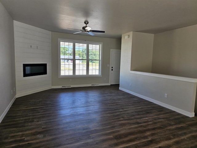 unfurnished living room featuring ceiling fan, a fireplace, and dark wood-type flooring