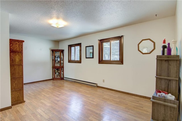 spare room featuring a textured ceiling, baseboard heating, and light hardwood / wood-style flooring