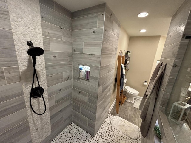 bathroom with toilet, a tile shower, and tile patterned flooring