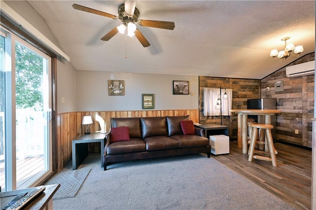 living room with vaulted ceiling, ceiling fan with notable chandelier, a textured ceiling, wood-type flooring, and wooden walls