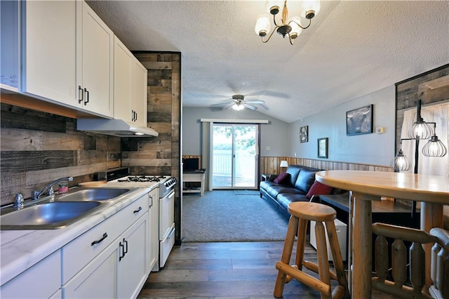 kitchen with dark wood-type flooring, ceiling fan with notable chandelier, white cabinets, wooden walls, and white gas range