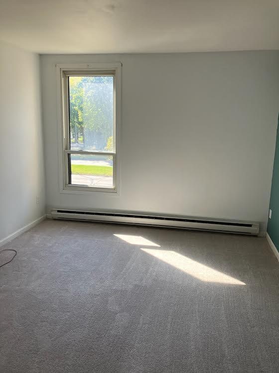 carpeted empty room featuring a baseboard radiator