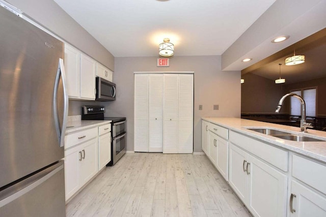 kitchen featuring pendant lighting, white cabinets, sink, light hardwood / wood-style floors, and stainless steel appliances