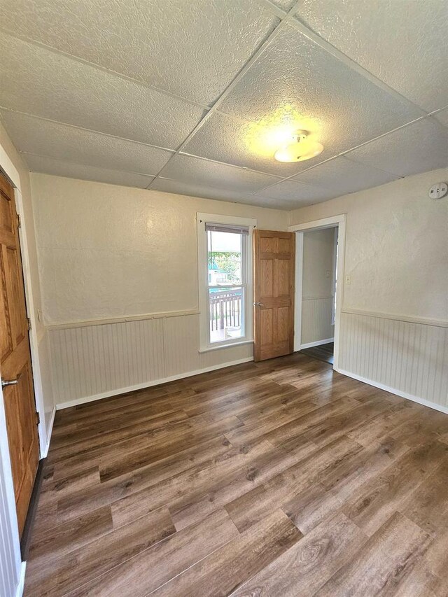 spare room with wood finished floors, a drop ceiling, and wainscoting