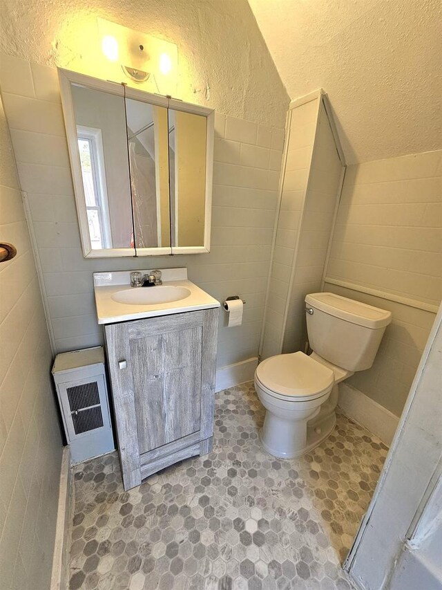bathroom featuring tile walls, a textured wall, toilet, and vanity