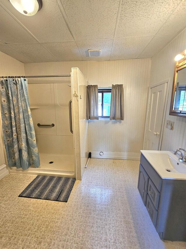 full bathroom featuring vanity, a shower stall, wooden walls, visible vents, and a paneled ceiling