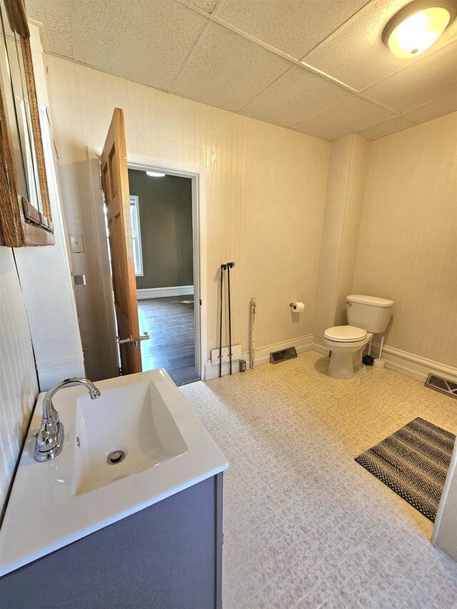 half bathroom featuring toilet, vanity, baseboards, visible vents, and a paneled ceiling