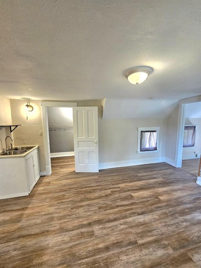 unfurnished living room featuring wood-type flooring, a textured ceiling, lofted ceiling, and sink