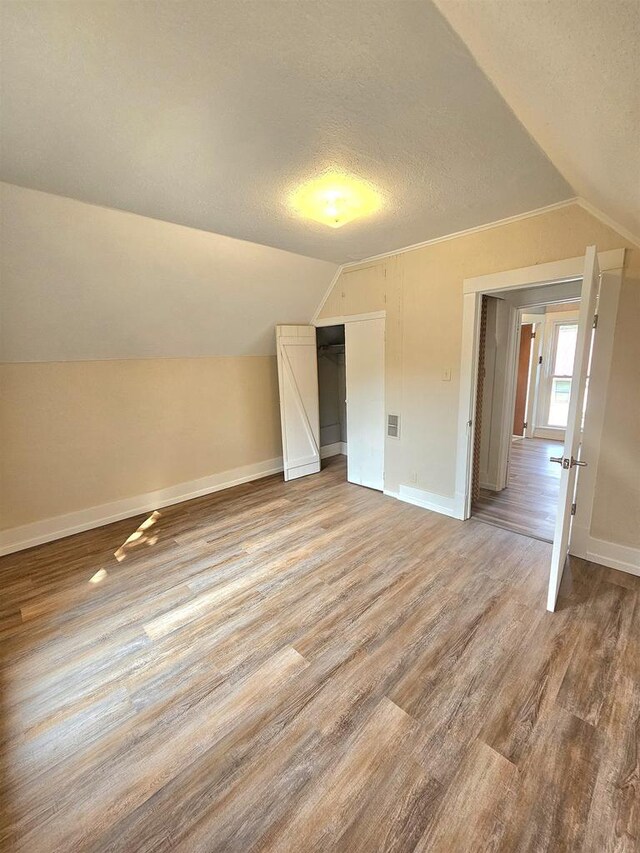 additional living space featuring baseboards, light wood-style floors, vaulted ceiling, and a textured ceiling