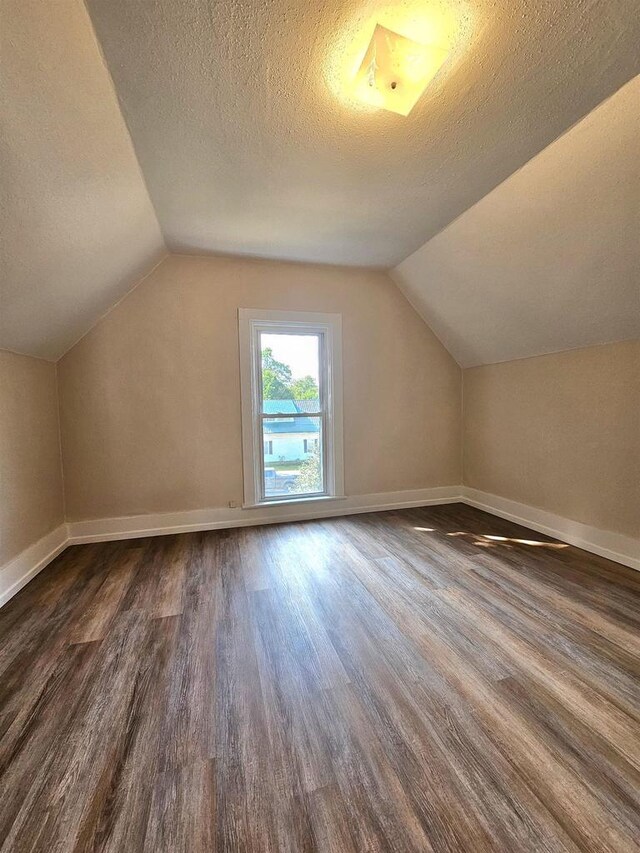 additional living space featuring a textured ceiling, baseboards, vaulted ceiling, and wood finished floors