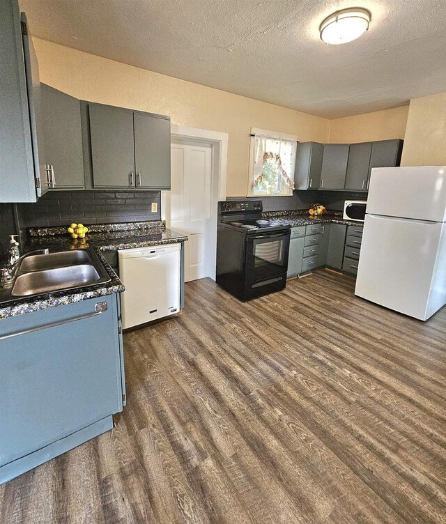 kitchen with gray cabinets, a sink, white appliances, dark countertops, and dark wood-style flooring