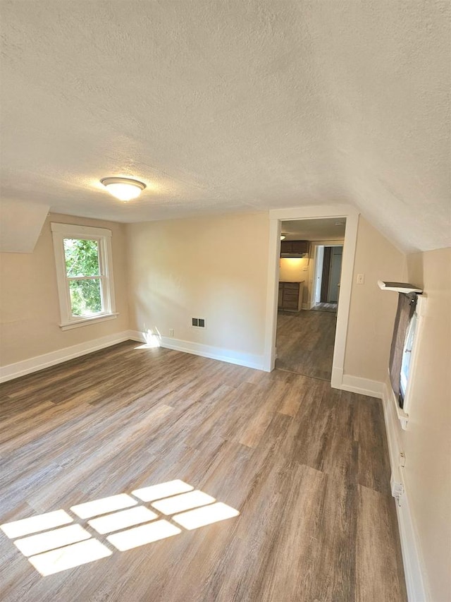 unfurnished living room featuring wood-type flooring, vaulted ceiling, and a textured ceiling