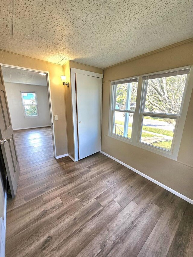 unfurnished bedroom featuring a closet, baseboards, a textured ceiling, and wood finished floors