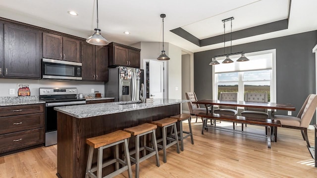 kitchen featuring light hardwood / wood-style floors, light stone countertops, stainless steel appliances, dark brown cabinets, and a center island with sink