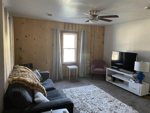 carpeted living room with ceiling fan and wood walls