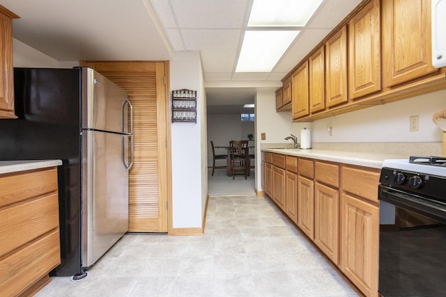 kitchen with stainless steel refrigerator, range with gas cooktop, a drop ceiling, and sink