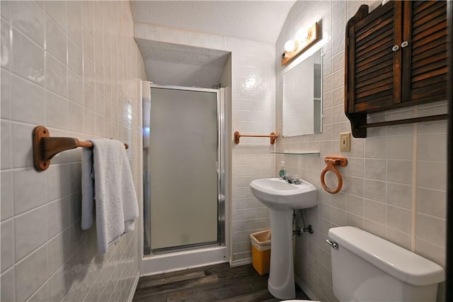 bathroom featuring tile walls, a shower with shower door, a textured ceiling, hardwood / wood-style floors, and toilet