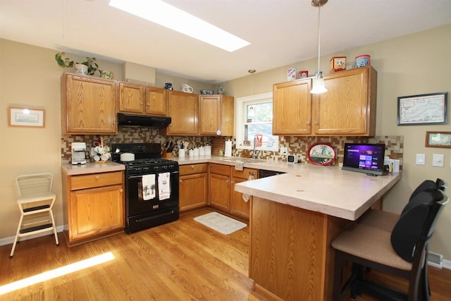 kitchen featuring black gas stove, hanging light fixtures, sink, kitchen peninsula, and decorative backsplash