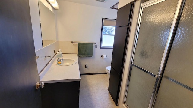 bathroom featuring a shower with door, vanity, and toilet