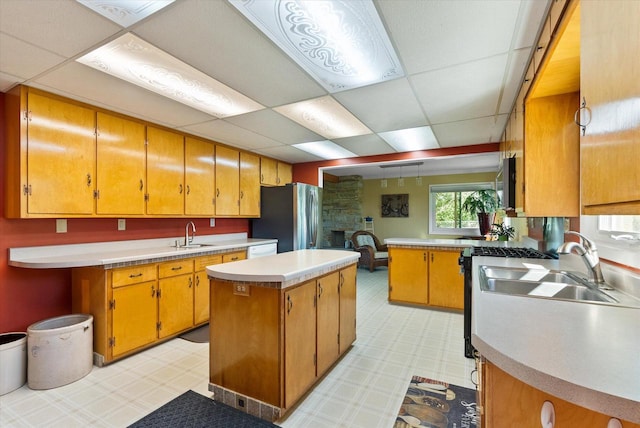 kitchen featuring stainless steel fridge, a kitchen island, sink, and a paneled ceiling