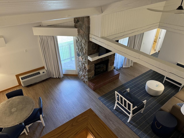 living room with lofted ceiling with beams, a wall mounted AC, hardwood / wood-style floors, and a stone fireplace