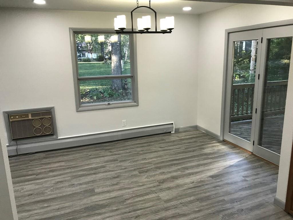 unfurnished dining area with baseboard heating, an AC wall unit, an inviting chandelier, and dark wood-type flooring