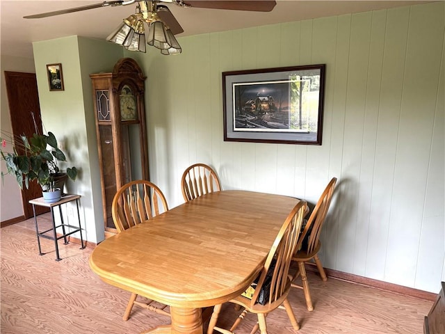 dining space with ceiling fan, wooden walls, and light hardwood / wood-style floors