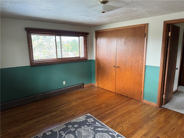 unfurnished bedroom with a baseboard radiator, hardwood / wood-style floors, and a closet