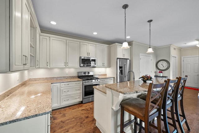 kitchen with dark wood-type flooring, an island with sink, white cabinets, hanging light fixtures, and appliances with stainless steel finishes