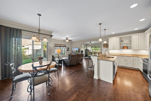 kitchen featuring dark stone counters, sink, ceiling fan with notable chandelier, a center island with sink, and decorative light fixtures