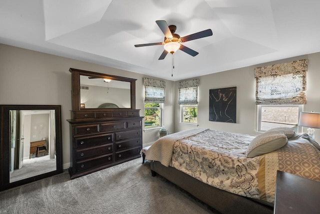 carpeted bedroom with a raised ceiling and ceiling fan