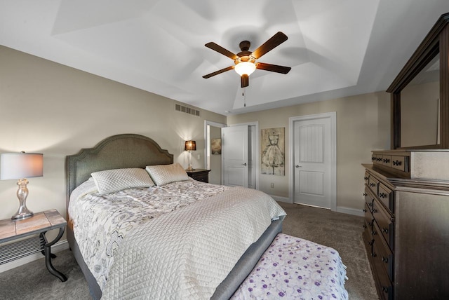 bedroom featuring a tray ceiling, dark carpet, and ceiling fan