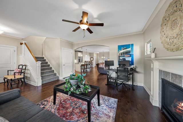 living room with ceiling fan with notable chandelier, crown molding, dark wood-type flooring, and a tile fireplace