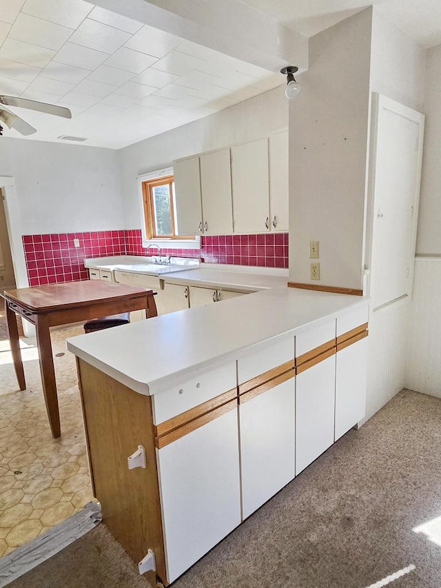 kitchen with ceiling fan, backsplash, kitchen peninsula, and white cabinetry