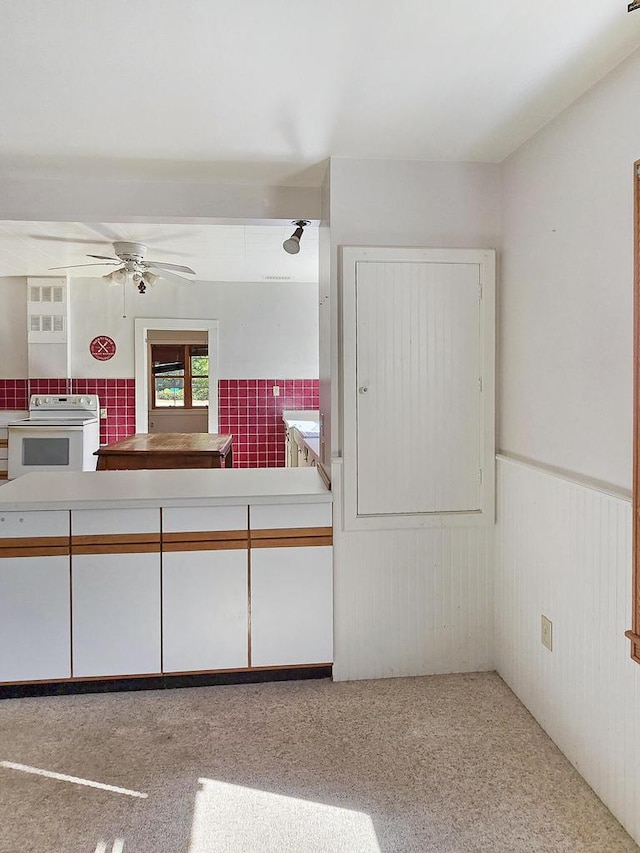 kitchen with wood walls, white range with electric cooktop, ceiling fan, and white cabinets