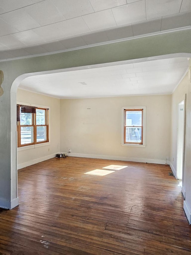 empty room featuring ornamental molding, dark wood-type flooring, and plenty of natural light