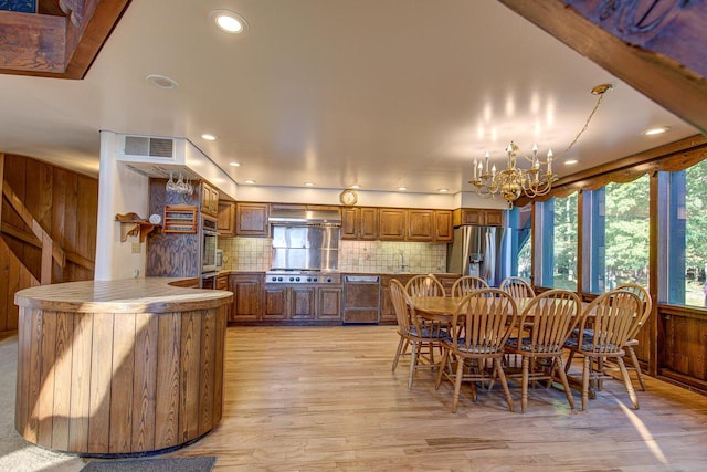 dining area with sink, light hardwood / wood-style flooring, wooden walls, and an inviting chandelier