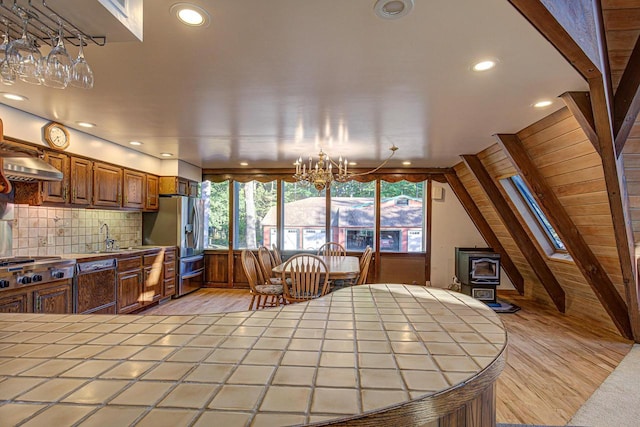 kitchen featuring tile counters, a wood stove, lofted ceiling with beams, pendant lighting, and a chandelier