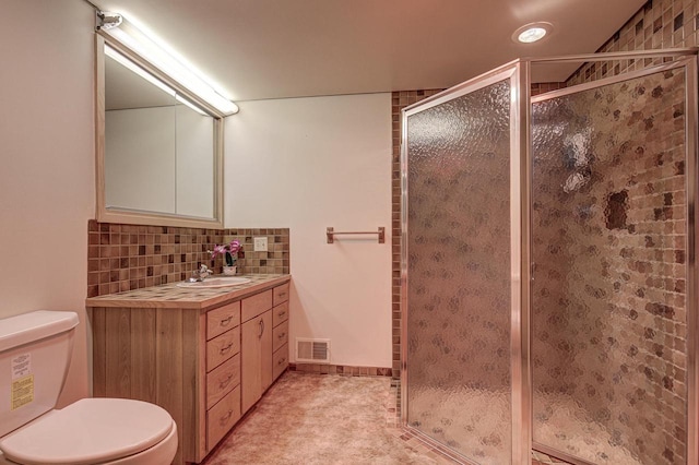 bathroom featuring a shower with door, vanity, backsplash, and toilet