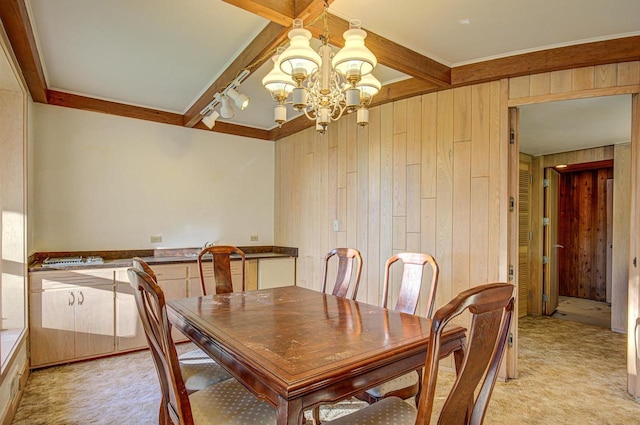 carpeted dining room with beam ceiling, track lighting, an inviting chandelier, and wooden walls