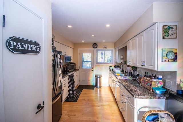 kitchen with sink, white cabinetry, appliances with stainless steel finishes, light hardwood / wood-style floors, and decorative backsplash