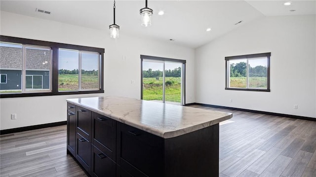 kitchen featuring light wood-type flooring, a center island, lofted ceiling, hanging light fixtures, and light stone countertops